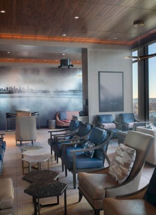 A modern lounge with plush seating, large windows overlooking water and a cityscape mural on the wall, creating a relaxing atmosphere.