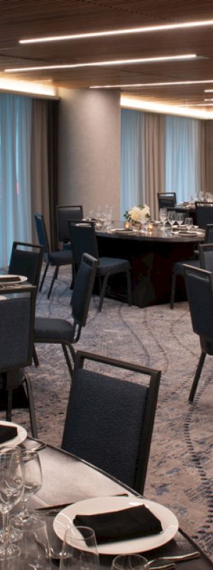 The image shows an elegant banquet hall with round tables, set with black napkins, glassware, and centerpieces, ready for an event.