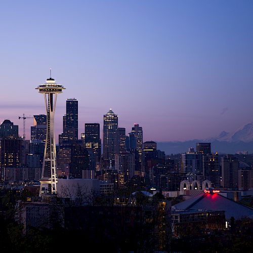 Seattle skyline at dusk with the Space Needle and Mount Rainier in the background, city lights starting to illuminate the scene.
