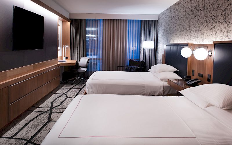 A modern hotel room with two beds, a flat-screen TV, desk, and stylish decor.